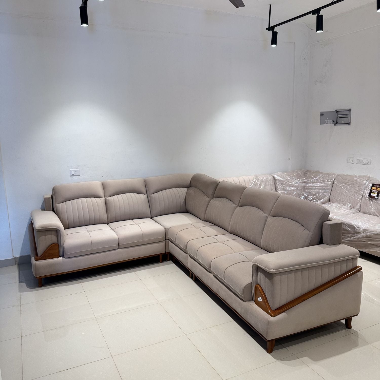 Beige sectional sofa in a showroom setting with white walls and tiled floor.